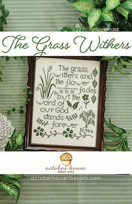 Framed cross stitch sampler featuring a Bible verse about the grass withering and the word of God standing forever, stitched with green grasses, flowers, and decorative motifs.