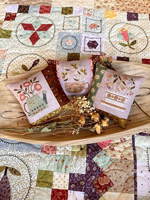 The Potting Bench #2 cross stitch pattern by Blueberry Ridge Designs featuring a detailed garden potting bench scene with plants, tools, rustic elements, and three small coordinating pillow designs included.