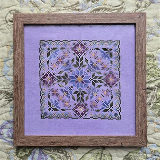Framed cross-stitched floral design on purple fabric with a wooden frame.