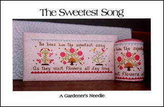 A horizontal cross stitch sampler featuring two small birds surrounded by pink flowers, green vines, and decorative motifs, stitched in soft pastel tones with a coordinating floral pin pillow shown beside the finished piece.