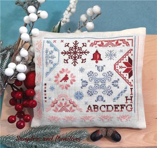 Decorative pillow with cross-stitch patterns on a wooden surface with festive elements.