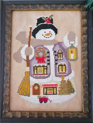 Framed cross-stitched snowman with a house design on a beige background