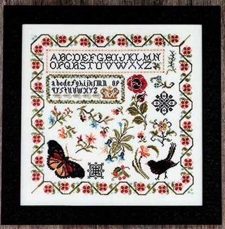 Framed cross stitch sampler featuring an alphabet at the top with birds, butterflies, floral motifs, and a decorative border in a multicolor palette.