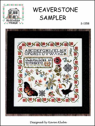Framed cross stitch sampler featuring an alphabet at the top with birds, butterflies, floral motifs, and a decorative border in a multicolor palette.