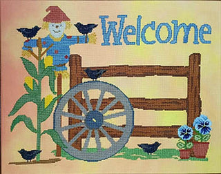 Cross stitch design featuring a blue scarecrow among corn stalks with blackbirds, a rustic fence, wagon wheel, and blue flower pot under the word “Welcome.”