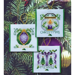 Set of cross-stitched Christmas ornaments on a green leafy background