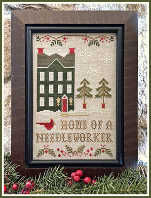 Cross stitch design featuring a snow-covered house, winter trees, and the phrase “Home of a Needleworker” stitched in gold, by Little House Needleworks.