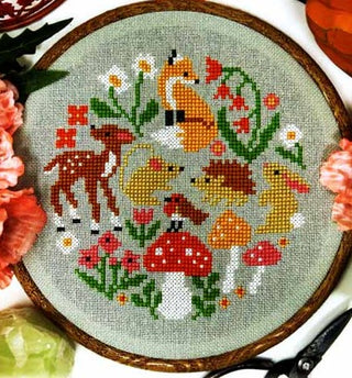 Cross-stitched design of forest animals and plants on a green fabric background.