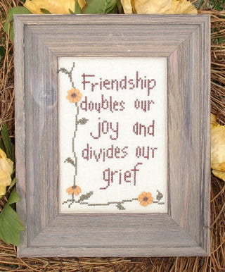 Cross stitch design with friendship quote framed by vines and peach flowers on a neutral background.