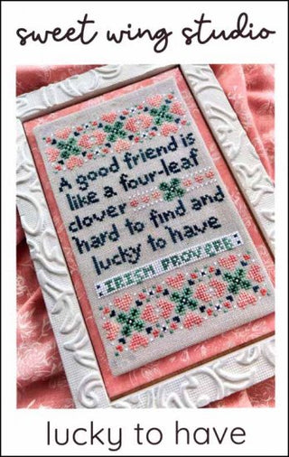 A cross stitch pattern chart with a four-leaf clover and text pattern, in a colorful embroidery format, in a clear plastic cover.